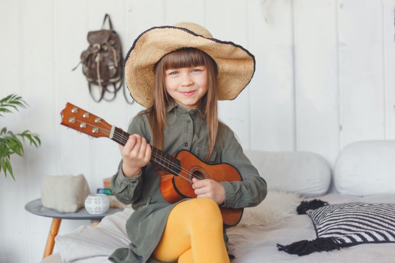 Kid girl in hat playing ukulele at home