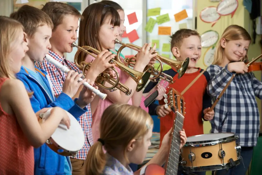 A group of children playing various musical instruments, including trumpets, flute, violin, tambourine, guitar, and drums, in a music lessons Westchase classroom setting with colorful notes on the walls.